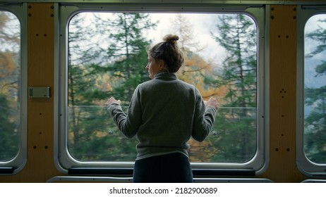 Cinematic and symmetrical beautiful shot of female traveler, travel blogger and inspired adventurer hang out of train window, look at amazing landscape of autumn mountains