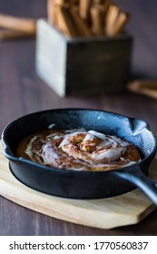 Cinnamon Bun Baked In A Cast Iron Skillet Topped With Icing Sugar.