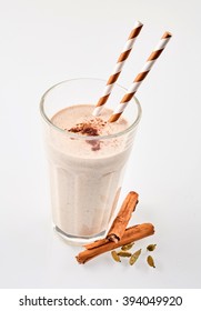 Cinnamon Chai Latte Smoothie Garnished With Cardomom Beside Herbs With Straws Over White Background