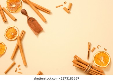 A lot of cinnamon (Cinnamomum) sticks scattered on a light background with cinnamon powder and some dried orange slices. Blank space to display product extracted from these herbals. Healthy concept