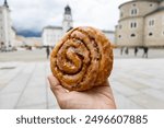 Cinnamon Roll Held in a Hand in Residenzplatz of Salzburg Austria