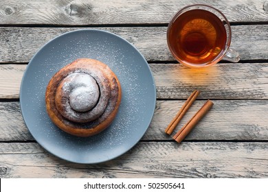 A Cinnamon Roll With Sugar And Cup Of Tea. Breakfast Food. Top View. Rustic Scene