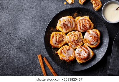 Rollos de canela, bollos, canela en un plato negro. Fondo oscuro. De cerca. Copiar espacio.