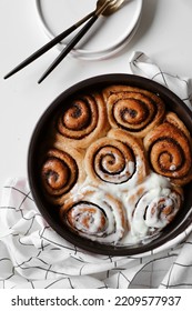 Cinnamon Rolls Covered With Mascarpone Cream, Chocolate And Nuts In Round Baking Dish, Appetizing Homemade Pastries, Sweet Baking Bun, Dessert Close Up, White Background, Flat Lay, Top View