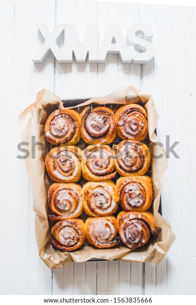 Cinnamon rolls\
with sugar icing  ready to be eaten for christmas holiday, top view\
over a rustic wooden  background  with a  giant xmas decoration of\
wooden atop, flat\
layout