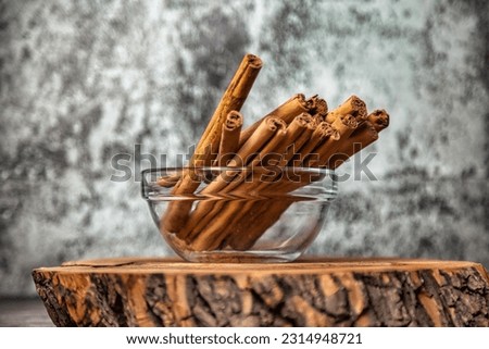 Cinnamon sticks in glass plate on wood board at grey textured wall, rustic style. Still life natural food of ceylon cinnamon sticks on wooden table. Delicious tasty healthy concept. Copy ad text space