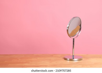 The circle shaped mirror setting on the desl with color background.