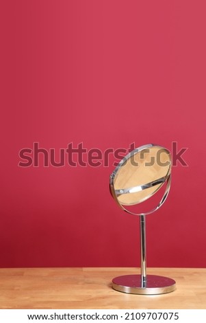 The circle shaped mirror setting on the desl with color background.