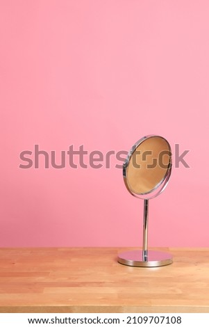 The circle shaped mirror setting on the desl with color background.