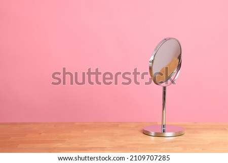 The circle shaped mirror setting on the desl with color background.