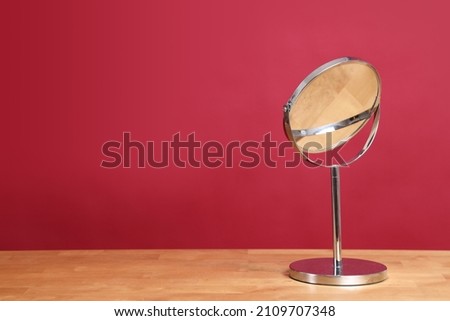 The circle shaped mirror setting on the desl with color background.