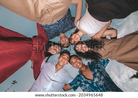 A circle of six young friends posing happily for the camera. Shot from the ground looking up. Friendship and teamwork concept.