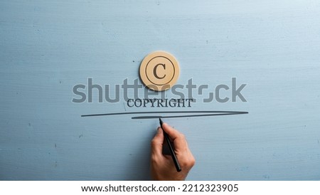 Circled letter C on a wooden cut circle with male hand writing a Copyright word under it. Over wooden blue background.