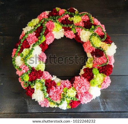circlet of carnation flowers on dark wooden background with copyspace
