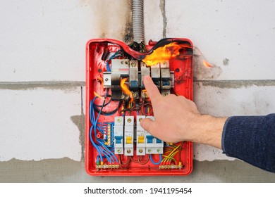 Circuit Breakers On Fire From Overheating Due To Poor Connection Or Poor Quality Wires. Finger Of Male Hand Turns Off Burning Switchboard From Overload Or Short Circuit On Wall. 