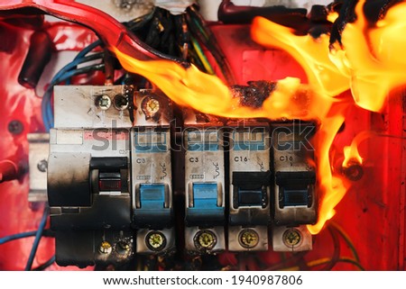 Circuit breakers on fire from overheating due to poor connection or faulty home wiring. Burning switchboard from overload or short circuit on wall close-up. Selective focus