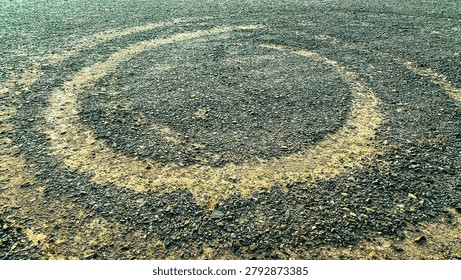 Circular  alien ufo marks create dark rings on a gravelly dirt surface with scattered rocks and rough texture forming a distinct pattern on the open ground outdoors