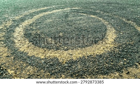 Circular  alien ufo marks create dark rings on a gravelly dirt surface with scattered rocks and rough texture forming a distinct pattern on the open ground outdoors