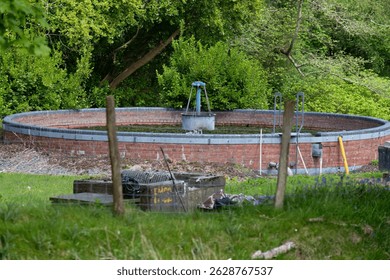 A circular brick structure, possibly a well or cistern, sits partially sunken in a grassy area shaded by trees. Trefor - Gwynedd - Lleyn Peninsula - Wales - Great Britain
