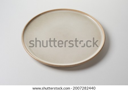 Circular clean generic pottery plate in a neutral beige on a white studio background in a high angle view for placement or styling of food for advertising