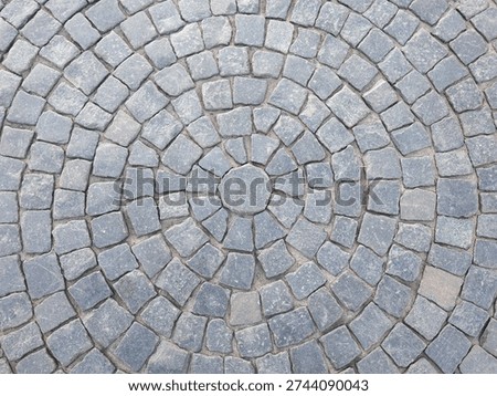 Circular cobblestone pavement pattern made of gray stone blocks, top view background texture, outdoor surface detail.