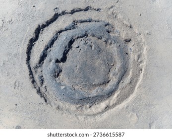 Circular depression in sandy beach with concentric swirls and ridges natural erosion pattern