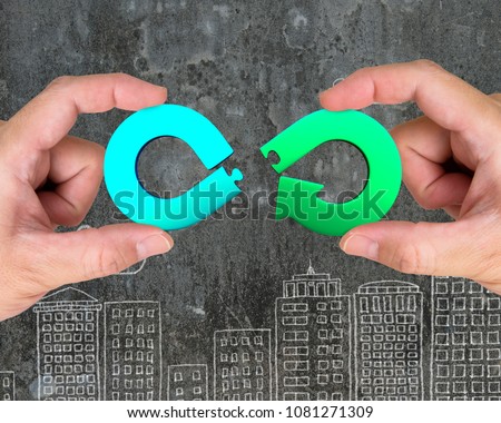 Circular economy concept. Two hands assembling arrow infinity recycling symbol of jigsaw puzzle pieces, on city buildings doodles background.