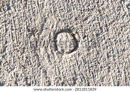 Circular indented mark pressed into a rough concrete surface with harsh shadow contrast