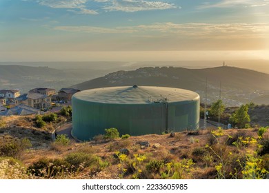 Circular large community water tank at San Marcos in San Siego, California. Water tank near the slope of a hill with bushes and shrubs against the houses and mountains at the back.
