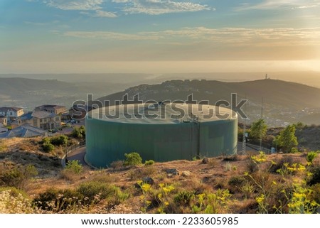 Circular large community water tank at San Marcos in San Siego, California. Water tank near the slope of a hill with bushes and shrubs against the houses and mountains at the back.