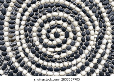 Circular mosaic paving pattern composed of smooth black and white river stones
