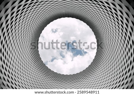 Circular opening in a modern architectural structure, revealing a view of the cloudy sky through a patterned, tunnel-like metallic design.