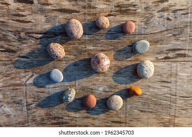 Circular pattern of multicolored pebbles on a gray old wooden surface. Spa decoration. Meditation and relaxation concept. Flat lay, top view