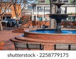 A circular red brick water fountain with benches, bare winter trees and a little girl running and parked cars at the Marietta Square in Marietta Georgia USA