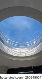 A circular view of the sky through a modern architectural structure, showcasing a railing and blue skies.