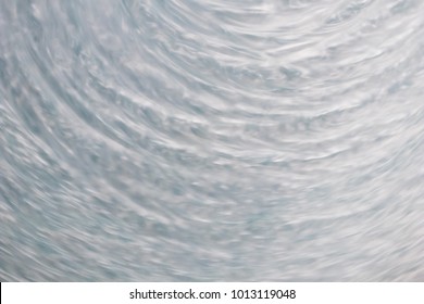 circular wave motion in a fluid system. blue gray background for a liquid pushed into a circular motion. waves and concentric circles with ripples as abstract and generic background. simulation of flu