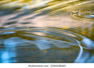 Circular wave rings reflecting sky and surrounding. Rain drops splashing into water surface causing concentric ripples. Bad weather conditions. Germany. Colorful macro close up with selective focus.