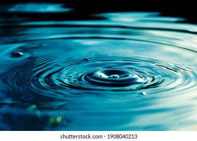 Circular Waves And Ripples In The Water From A Drop Falling. Natural Background Blue Water With Circles And Sky Reflection.