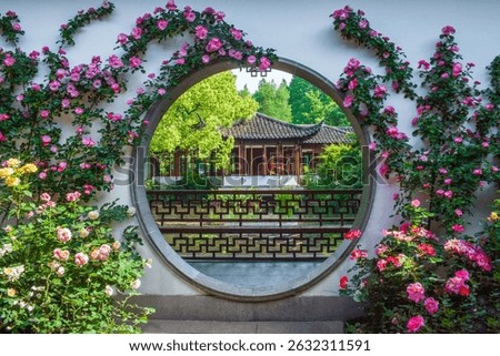A circular window framed with blooming pink roses offers a glimpse into a serene Chinese garden with a traditional pavilion.