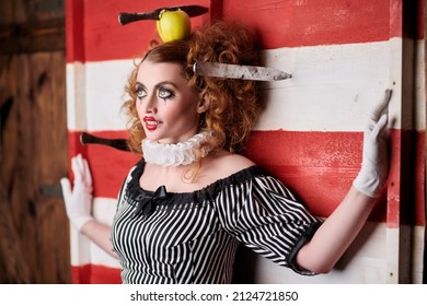 Circus performer girl in a clown costume performs a knife throwing trick. The dark circus concept. Retro style.