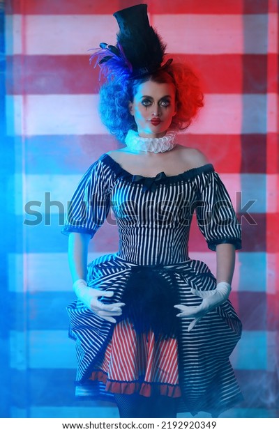 Circus performer\
girl in a clown costume performs a knife throwing trick. The dark\
circus concept. Retro\
style.