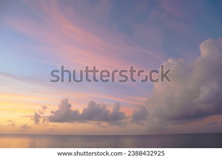 Cirrus clouds tinted pink by the sun at sunset over a calm blue ocean