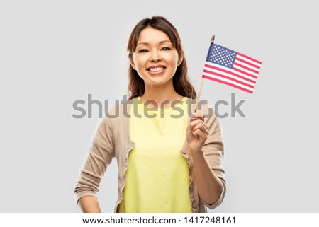 citizenship, ethnicity and independence day concept - happy asian young woman with american flag over grey background