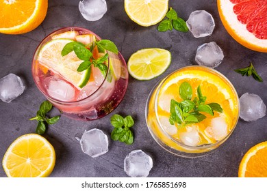 Citrus Cold Cocktail In Transparent Glasses On Dark Background. Around - Slices Of Orange, Lemon, Grapefruit, Ice And Mint. Top View, Flat Lay, Minimalism Concept Of Summer Citrus Soft Drink, Cocktail