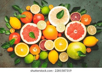 Citrus fruit food background, top view. Mix of different whole and sliced fruits: orange, grapefruit, lime and other with leaves on green table