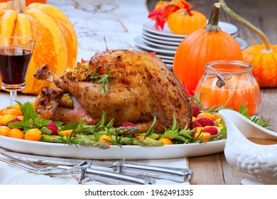 Citrus glazed roasted Turkey for Thanksgiving celebration garnished with kumquat, raspberry, asparagus, oregano, and fresh rosemary twigs. Holiday table decorated with pumpkins, candles, gourds