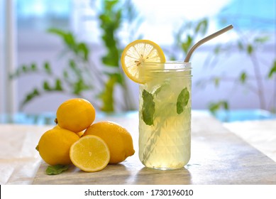 Citrus iced lemonade in pitcher and glasses with lemon slice and mint leaves decoration and on marble table on natural background. Fresh summer drink beautiful picture. Copy space