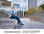 City break in Malmo Sweden. Beautiful middle-aged woman holding smart phone sitting on bench on promenade in city center of Malmo on autumn day. Side view