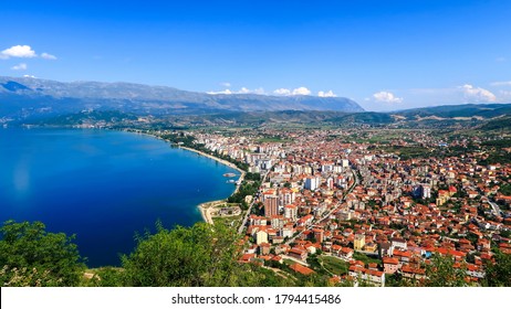 City buildings with red roofs at the shore of a lake with mountains in the background. View of Pogradec city and Ohrid lake, Pogradec, Albania. - Shutterstock ID 1794415486