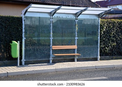 City Bus Stop. Glass Shelter With Integrated Wooden Bench. Only The Roof And The Back Wall. On The Street By The Sidewalk In The City. Elegant Arch, Station, Platform